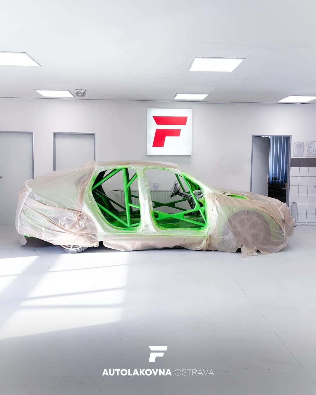 Závodní automobil s ochranným rámem lakovaným zářivě zelenou barvou v autolakovně